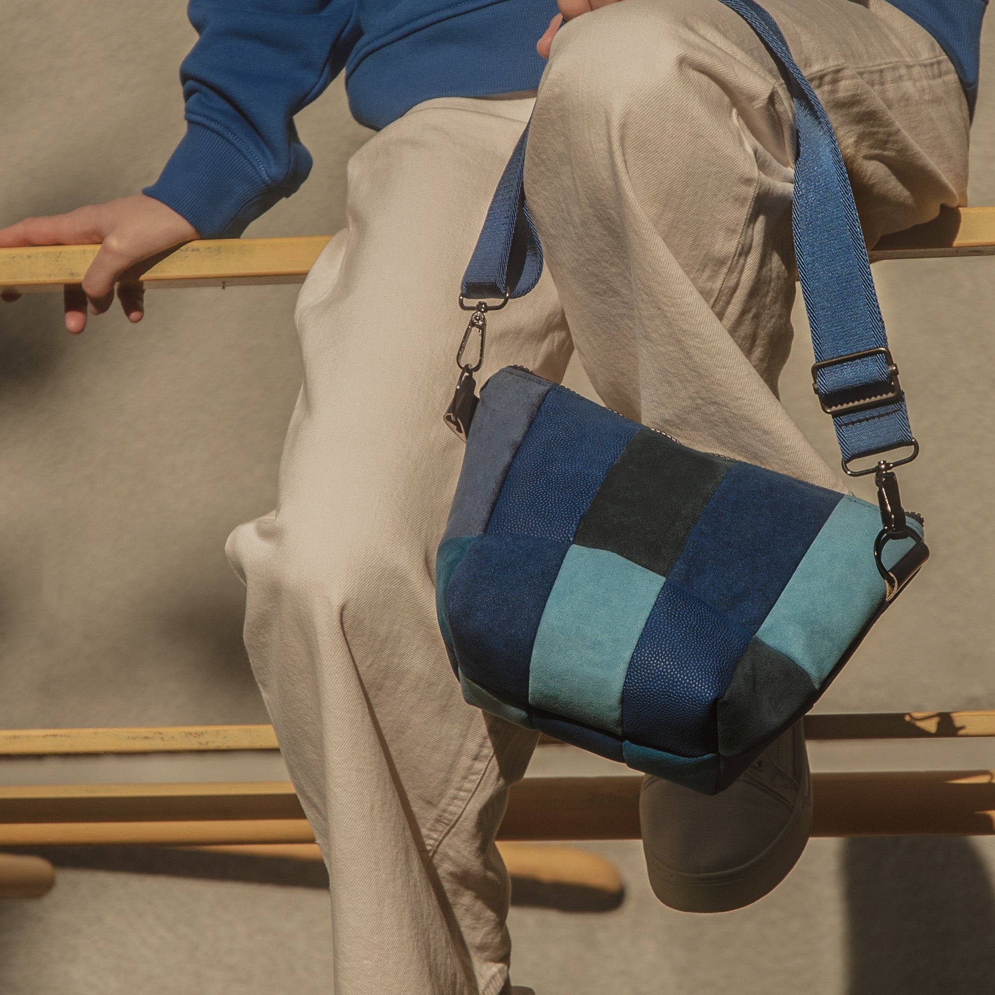 A person seated on a wooden structure holding a blue and white striped upcycled handbag.