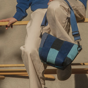 A person seated on a wooden structure holding a blue and white striped upcycled handbag.