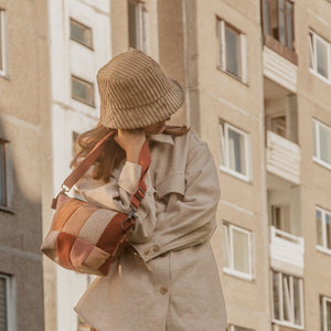 A person wearing a beige coat and a matching bucket hat, carrying a beige, red, and brown shoulder bag.
