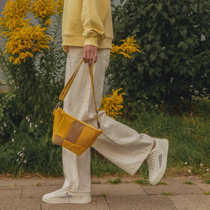 A person wearing a yellow sweater and white pants is holding a yellow and brown shoulder bag.