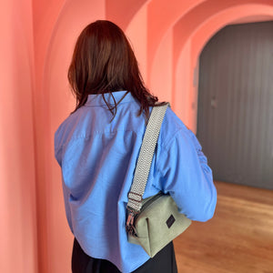 Person wearing a blue shirt and carrying a green bag in a pink architectural setting