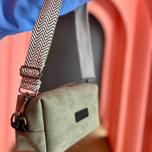 Green handbag with a herringbone strap held by a person wearing a blue shirt.