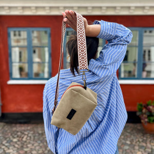 Person wearing a blue striped shirt with a beige crossbody bag in front of a red building.