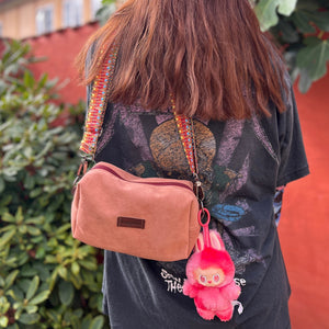 Person with a pink bag and pink monkey charm standing outdoors near greenery and a building.
