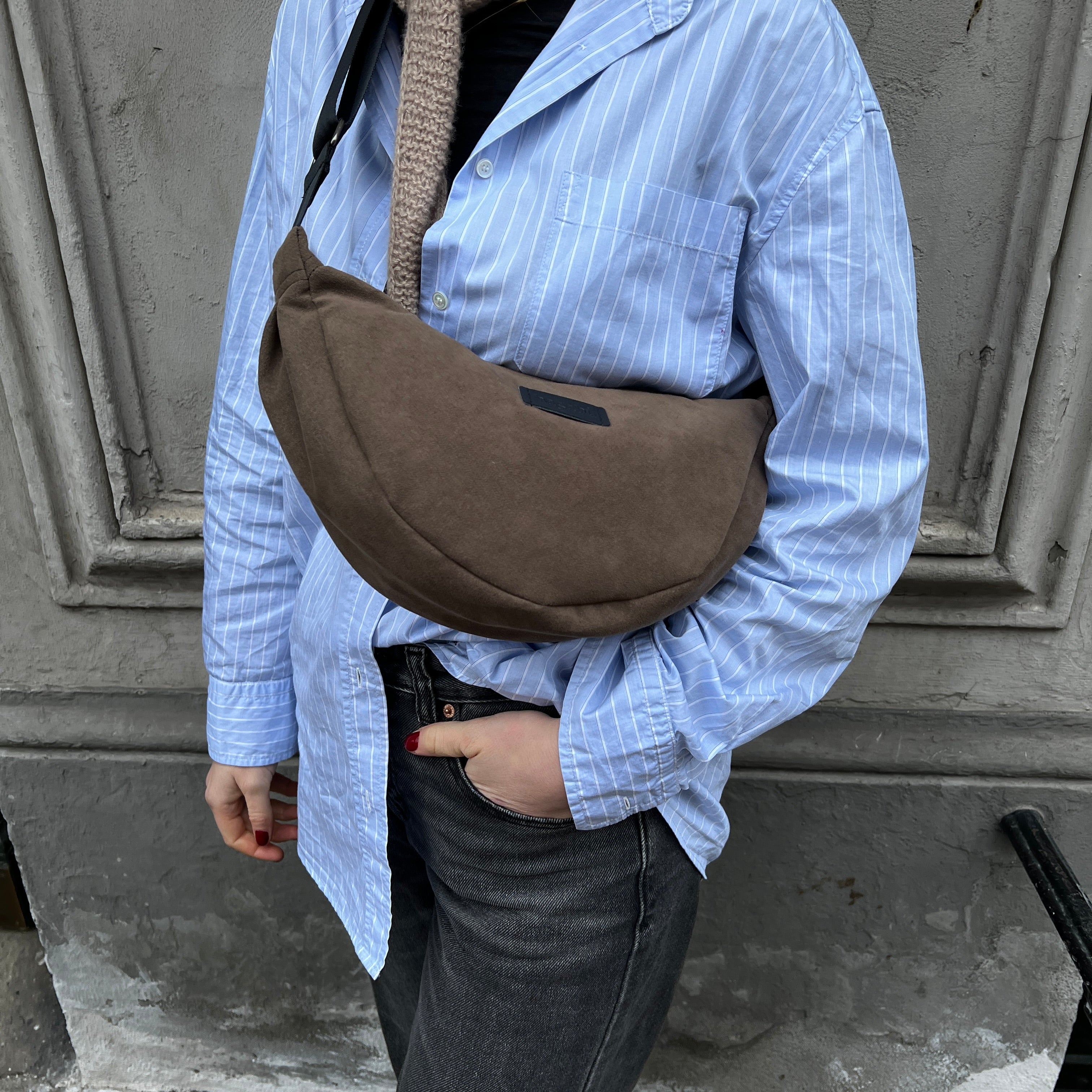 A person wearing a striped blue shirt and blue jeans, carrying a brown banana bag over their shoulder.