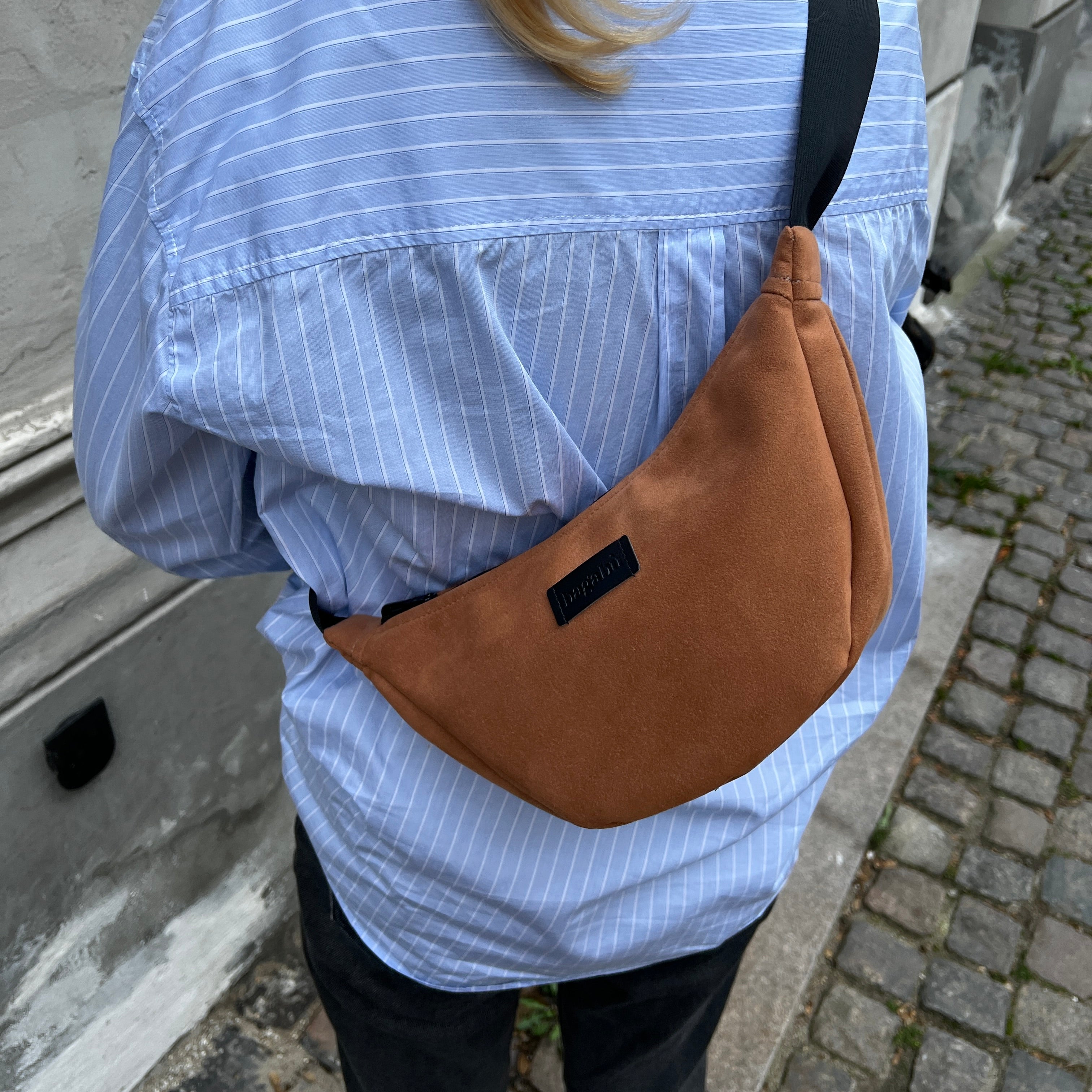 A person wearing a blue striped shirt with a brown banana-shaped handbag slung over their shoulder.