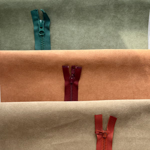 Three fabric rolls with zippers in green, red, and brown on a textured surface.
