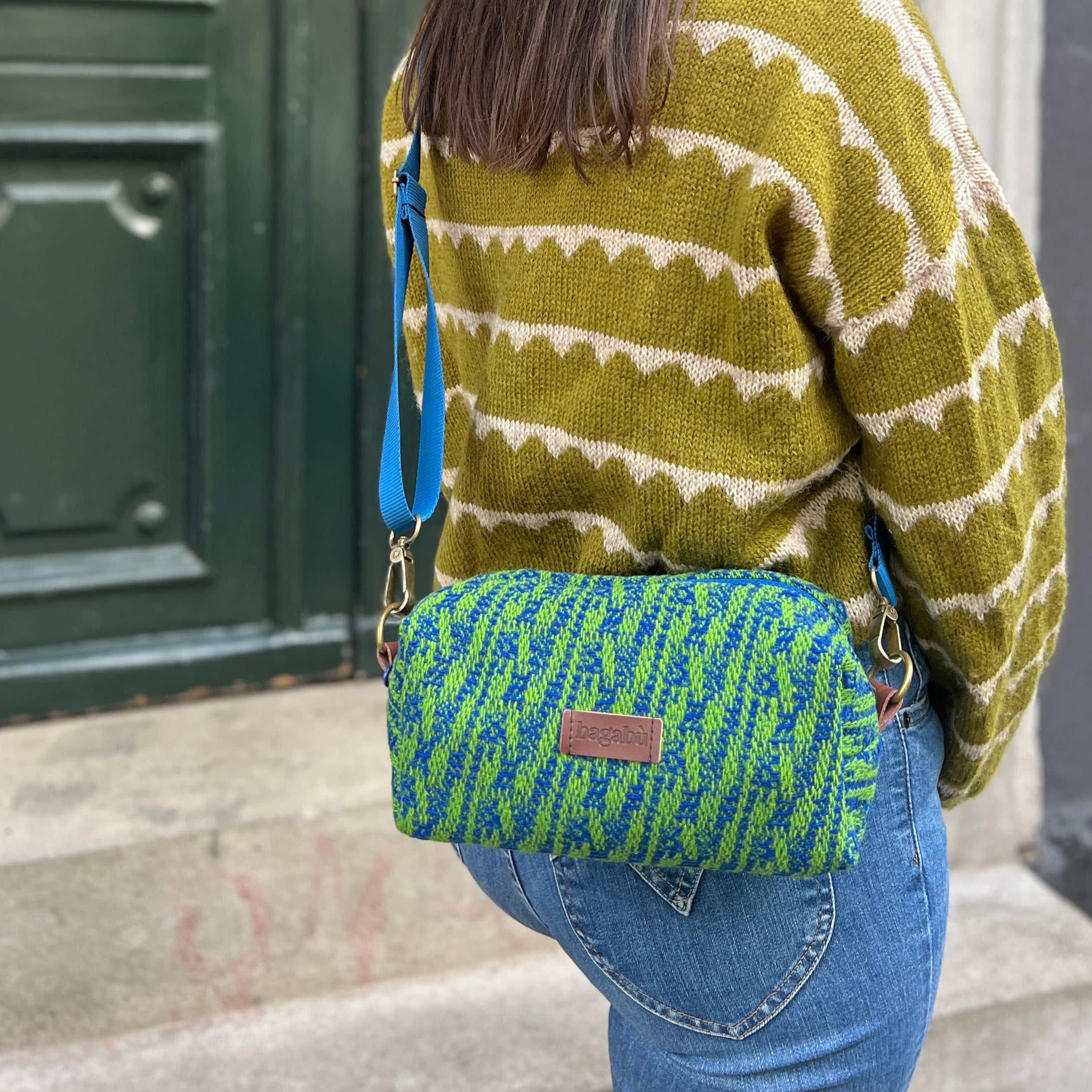 Woman wearing a green and white patterned sweater with a green and blue striped bag, standing in front of a green door.