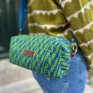 Green and blue patterned pouch held by a person wearing a green and white sweater.