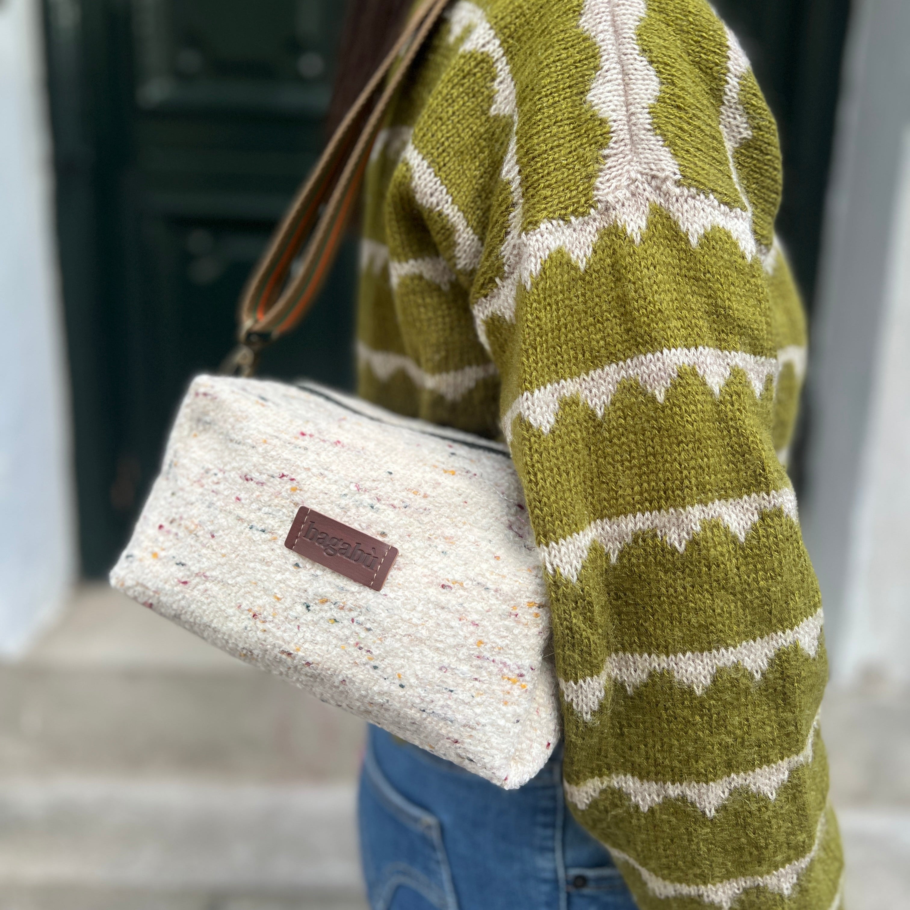 Person wearing a green and white patterned sweater holding a beige handbag.