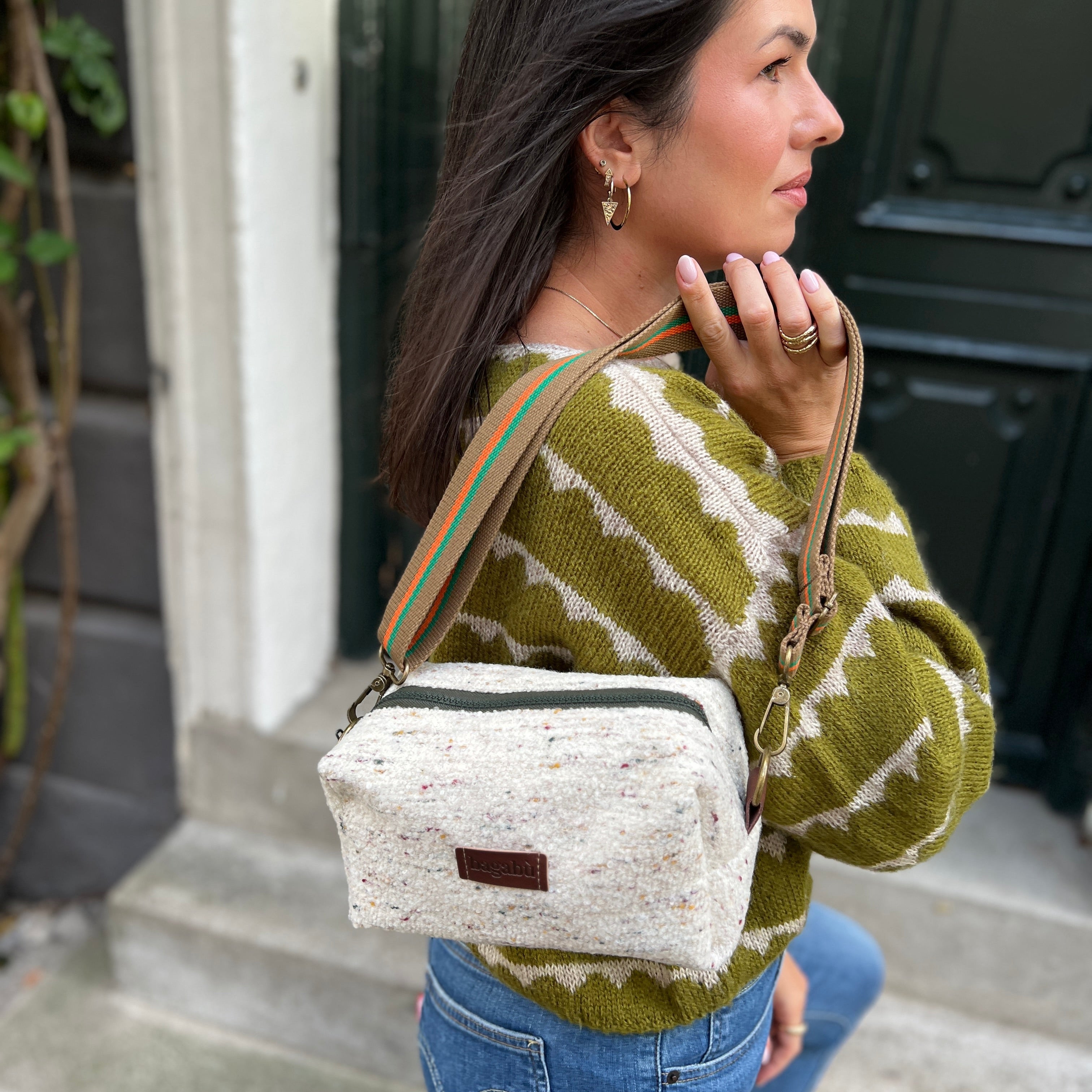 Woman wearing a green and white patterned sweater with a white bag, standing outdoors.