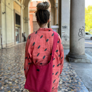 Person wearing a pink outfit with black patterns walking through an urban setting with columns and arches.