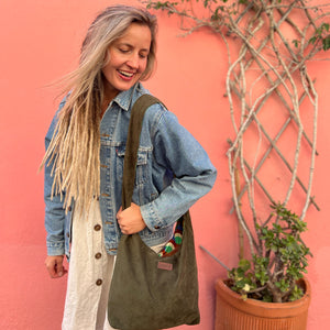 Woman holding a green bag against a pink wall with plants