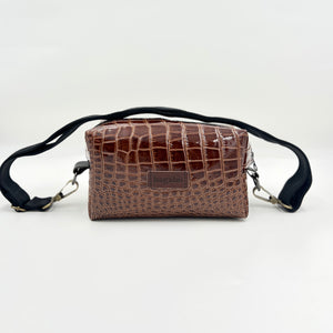 A brown leather shoulder bag with a textured pattern, featuring a black strap and a brand label on the front.