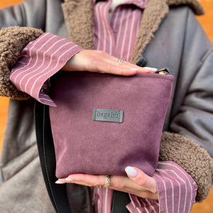 Person holding a purple bag with a visible brand logo against an orange background