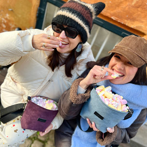 Two people eating colorful candies from containers, one wearing a striped hat and sunglasses, the other in a brown cap.