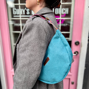 A person wearing a light blue banana-shaped handbag with a textured surface and a colorful strap.