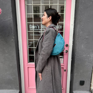 Person in gray coat with blue backpack standing by a pink door.