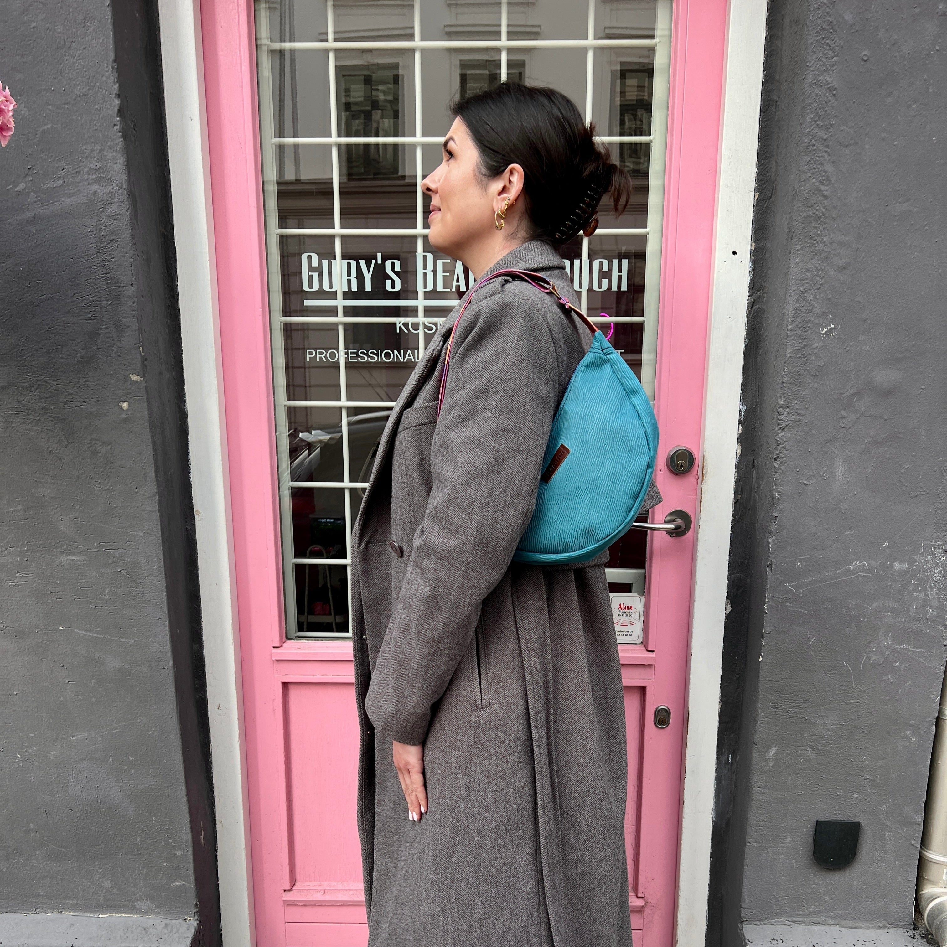 Person in gray coat with blue backpack standing by a pink door.