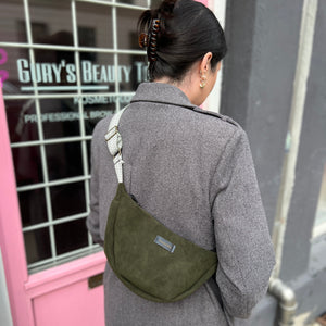 Person in gray coat with green bag walking past pink door.