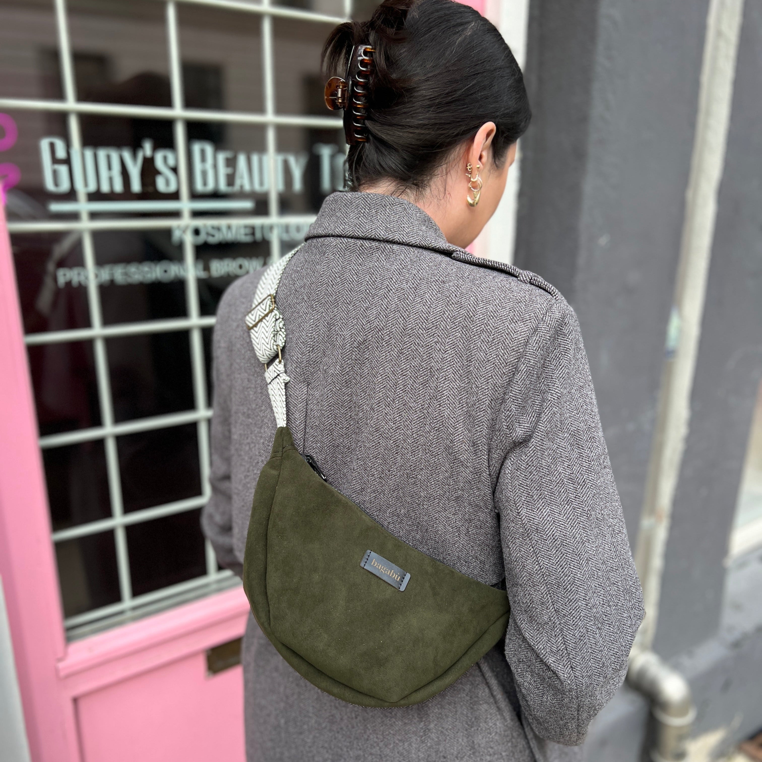 Person in gray coat with green bag walking past pink door.