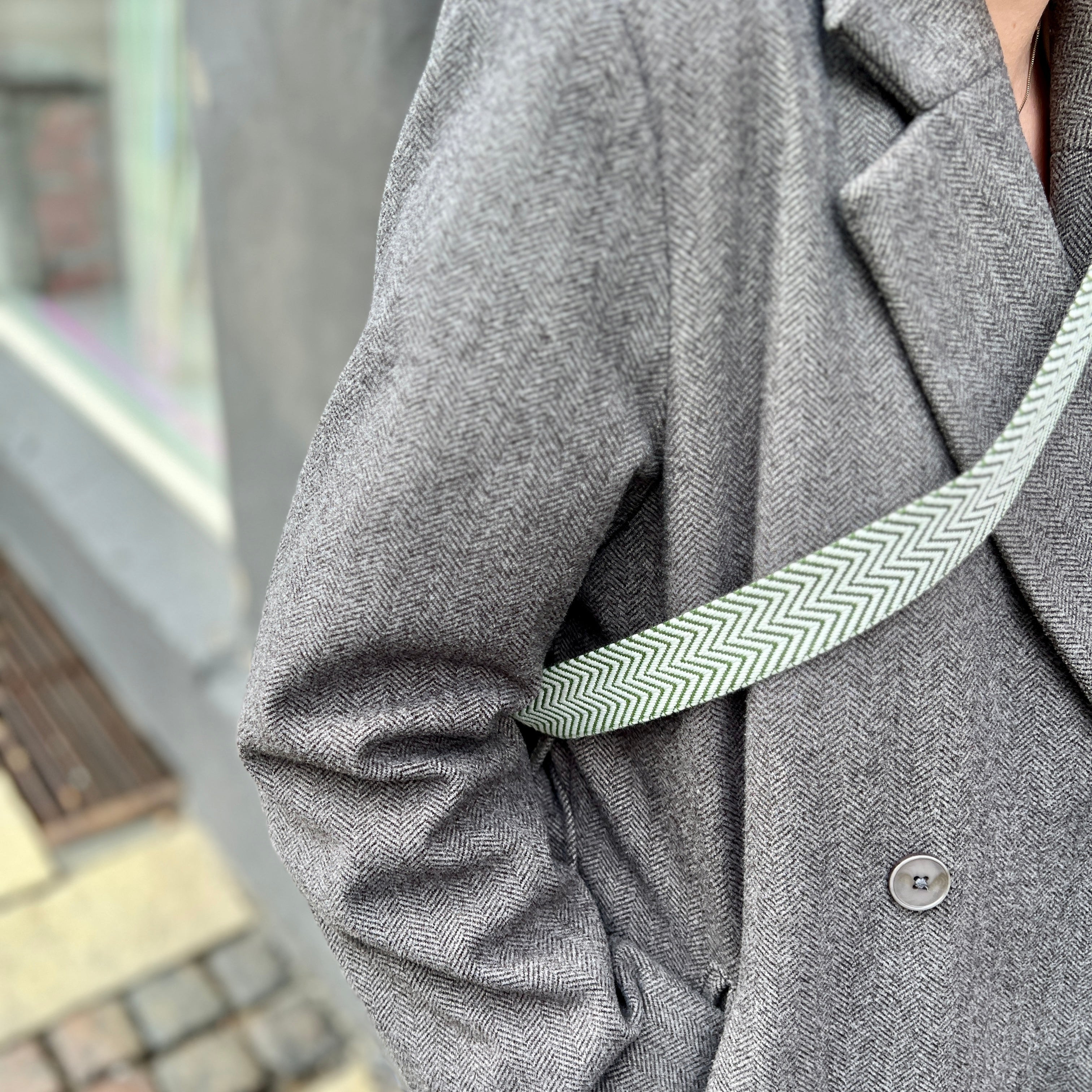 Person wearing a gray coat with a strap over shoulders.