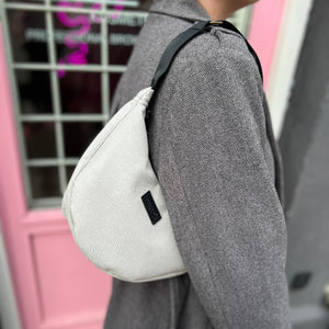 A person wearing a gray coat is carrying an off-white banana-shaped handbag over their shoulder.
