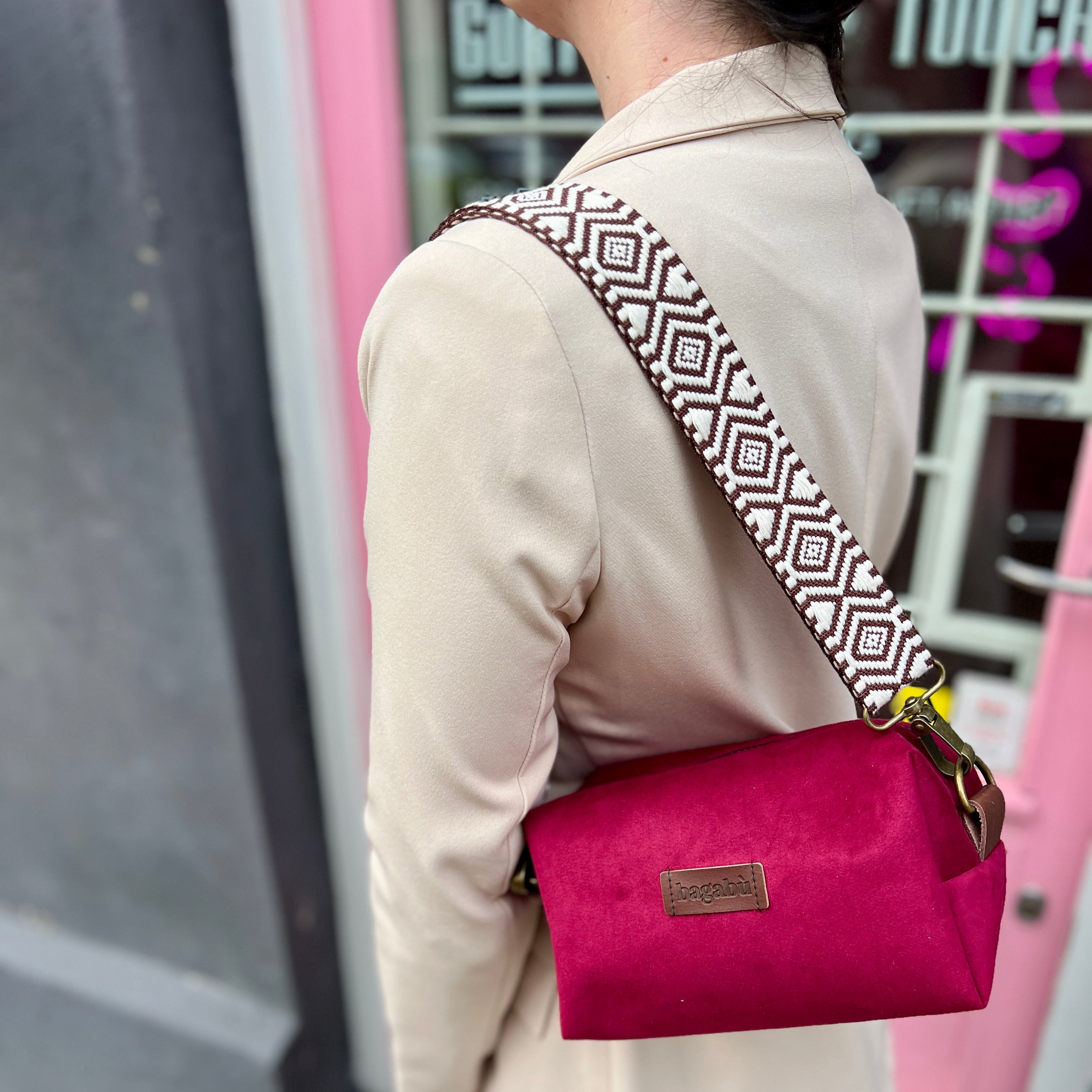 A person wearing a beige coat and carrying a fuchsia purple handbag with a geometric patterned strap over the shoulder.