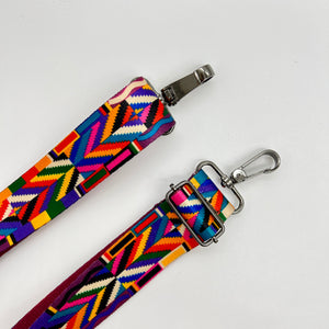 A multicolored geometric patterned adjustable shoulder strap with a metal clasp.