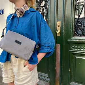 A person wearing a blue shirt and beige shorts, carrying a gray shoulder bag with a black strap, standing in front of a green door with a decorative handle.