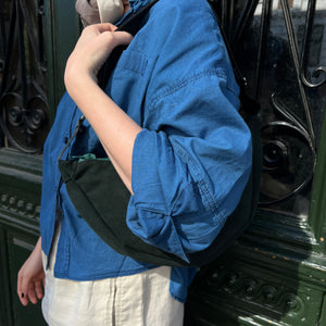 A person wearing a blue jacket and a dark green banana bag with a shoulder strap.