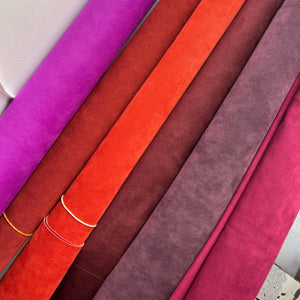 Rolls of purple, red, brown, and pink fabric on a white surface.