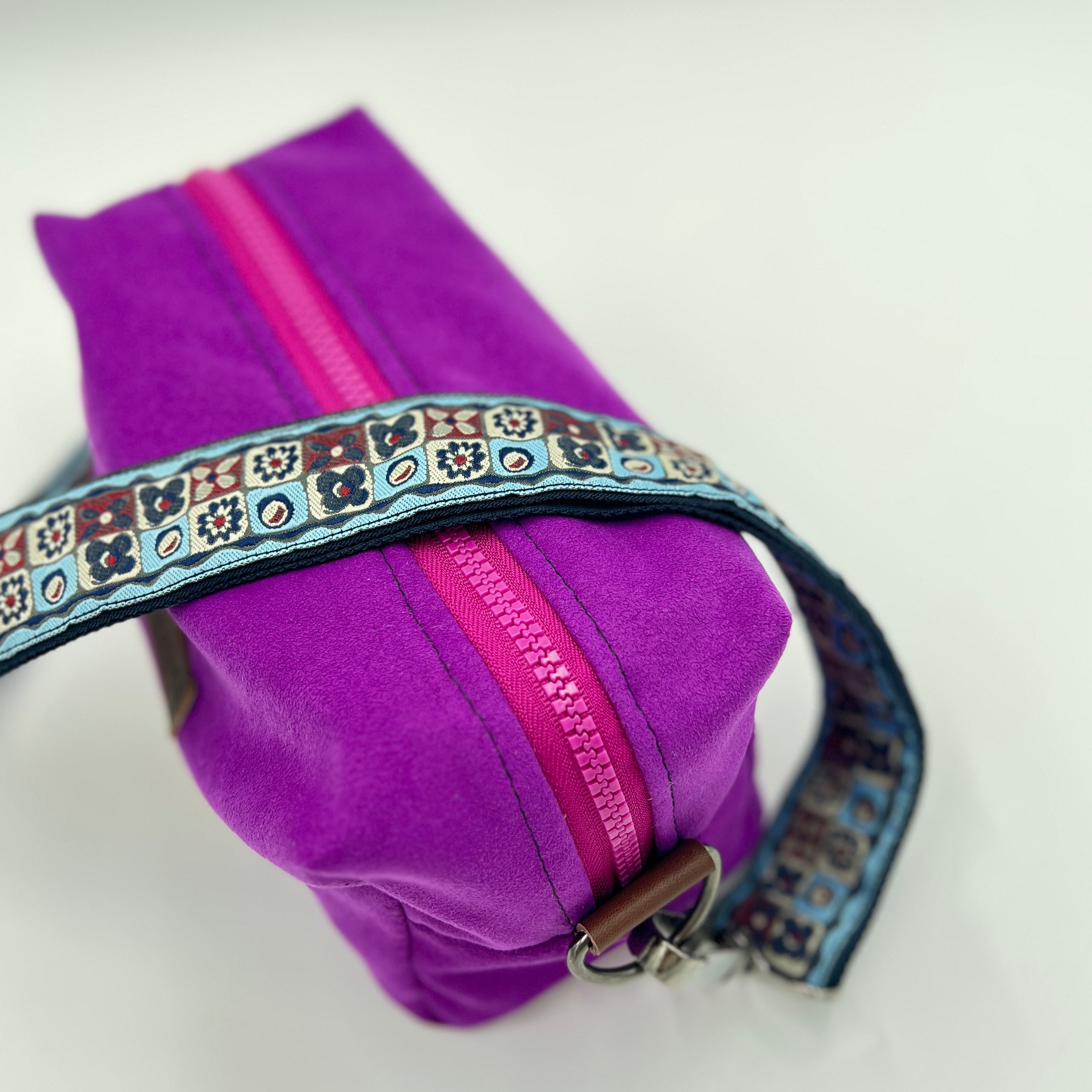 Purple pouch with a pink zipper and decorative strap on a white background