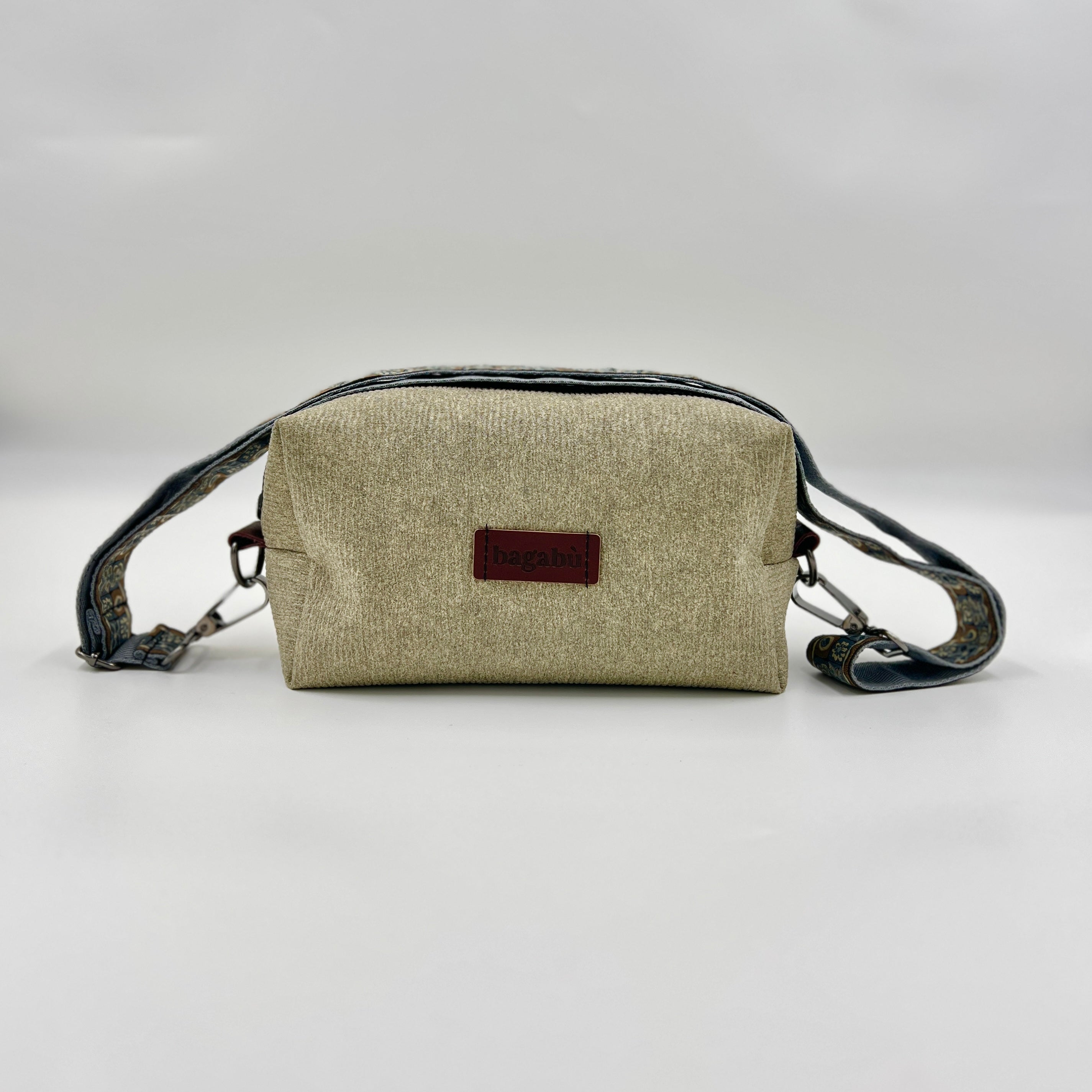 Beige crossbody bag with a brown label on a light gray background