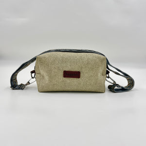 Beige crossbody bag with a brown label on a light gray background