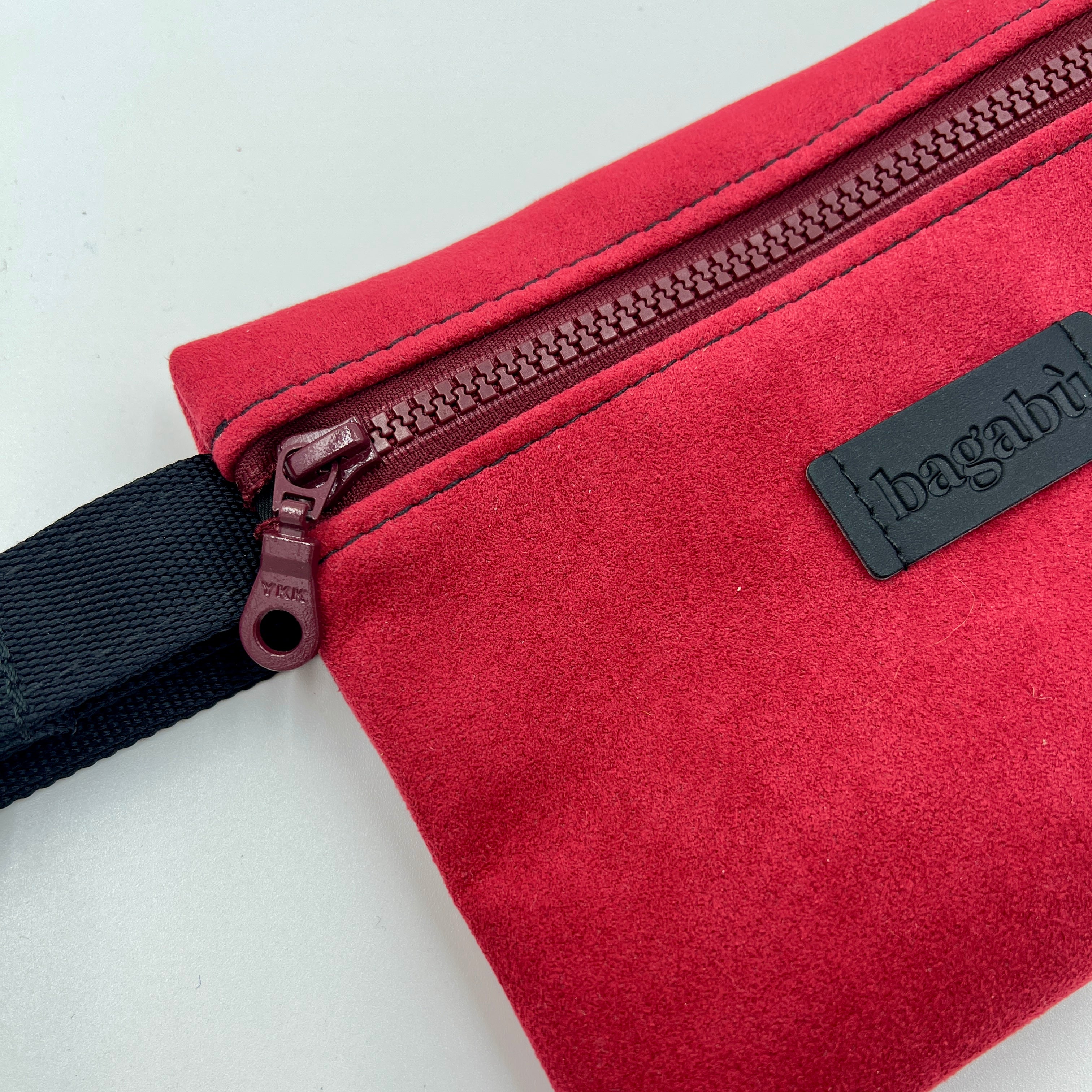 Red bag with a black strap and visible brand logo on a light gray background