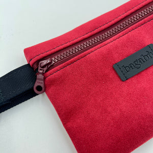 Red bag with a black strap and visible brand logo on a light gray background