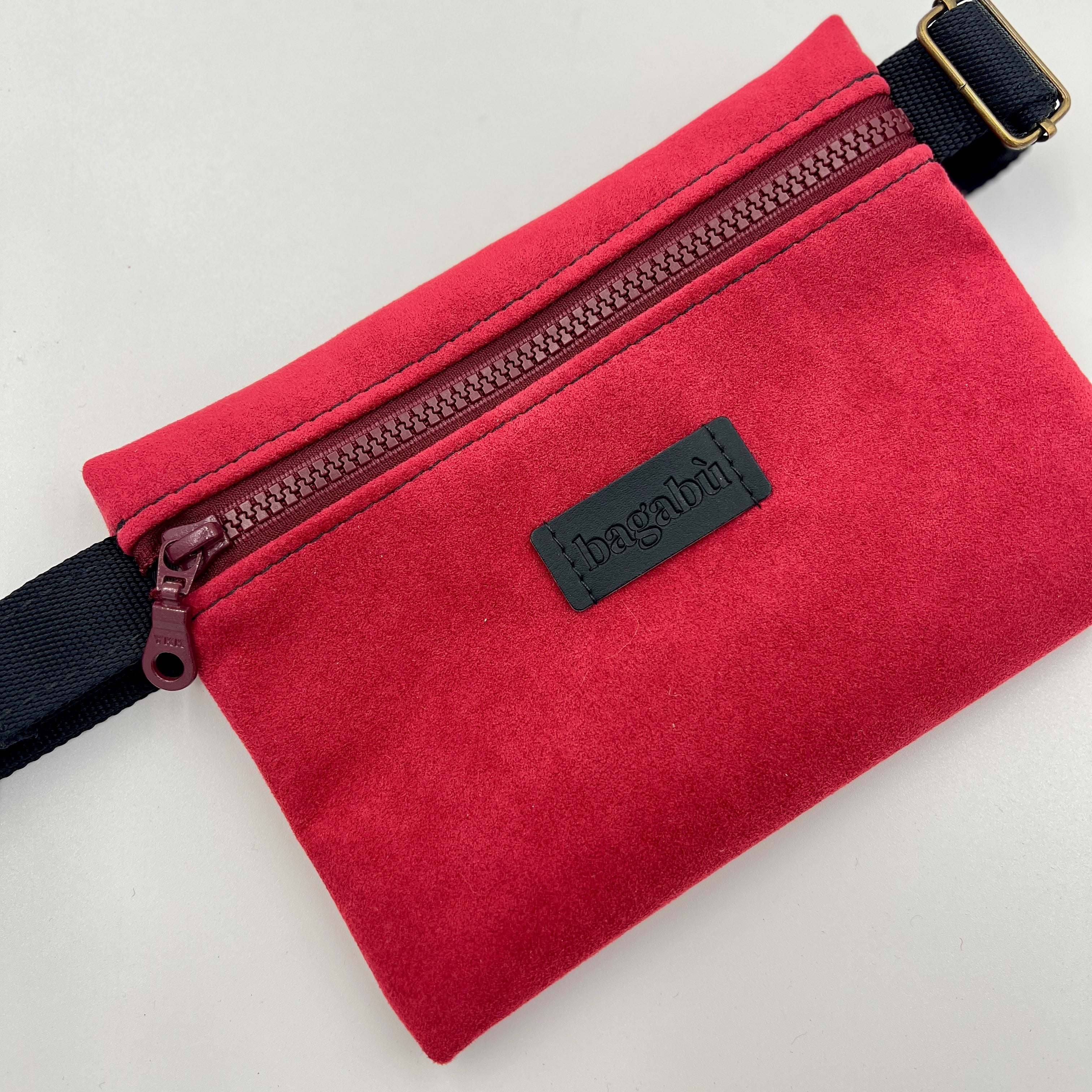 Red suede pouch with a zipper and black strap on a light gray background