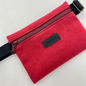 Red suede pouch with a zipper and black strap on a light gray background