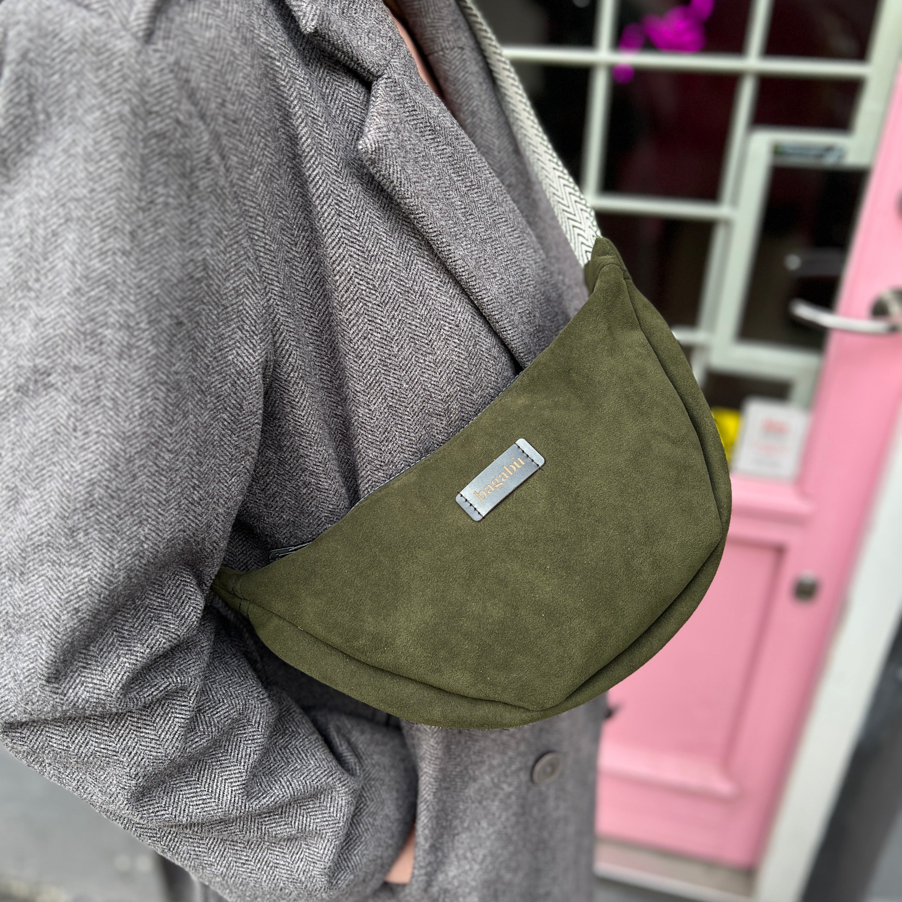 A person wearing a gray coat is holding a forest green banana bag.