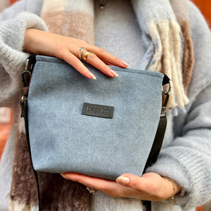 Person holding a blue crossbody bag with a visible brand logo, wearing a plaid scarf and gray coat.