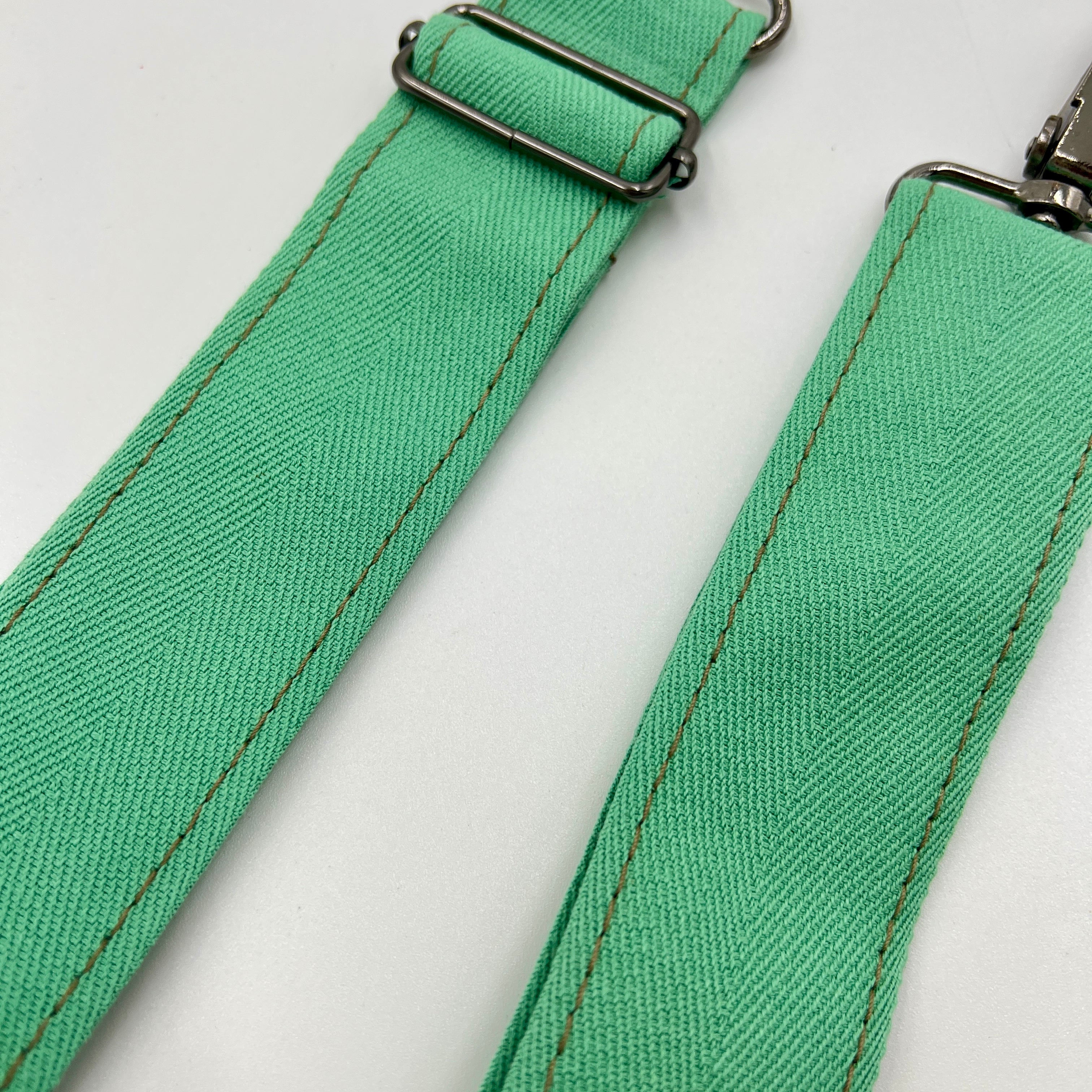 Close-up of a green fabric strap with metal clasps on a white background