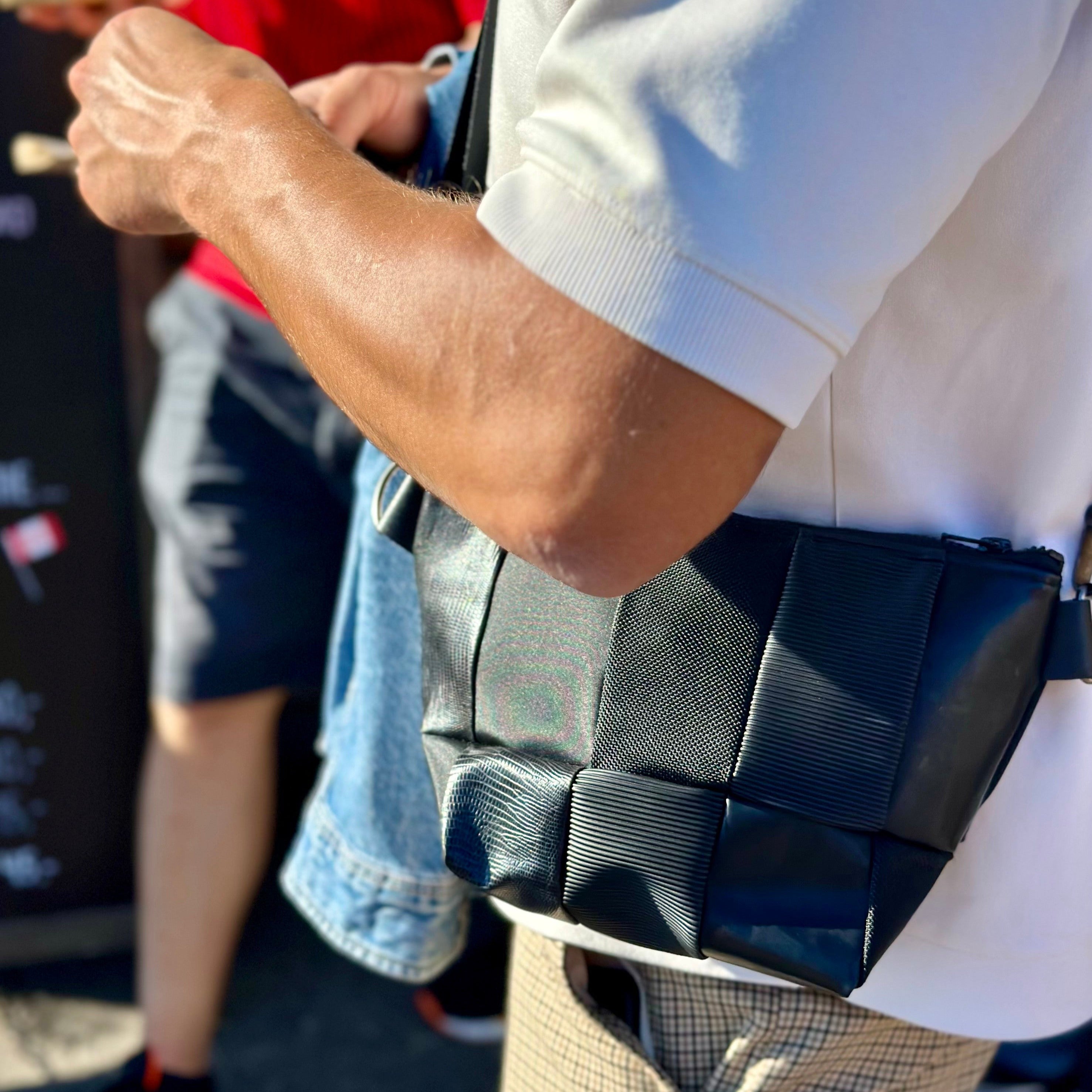 A person wearing a white shirt is holding a black, geometric-patterned bag across their body.