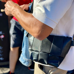 A person wearing a white shirt is holding a black, geometric-patterned bag across their body.