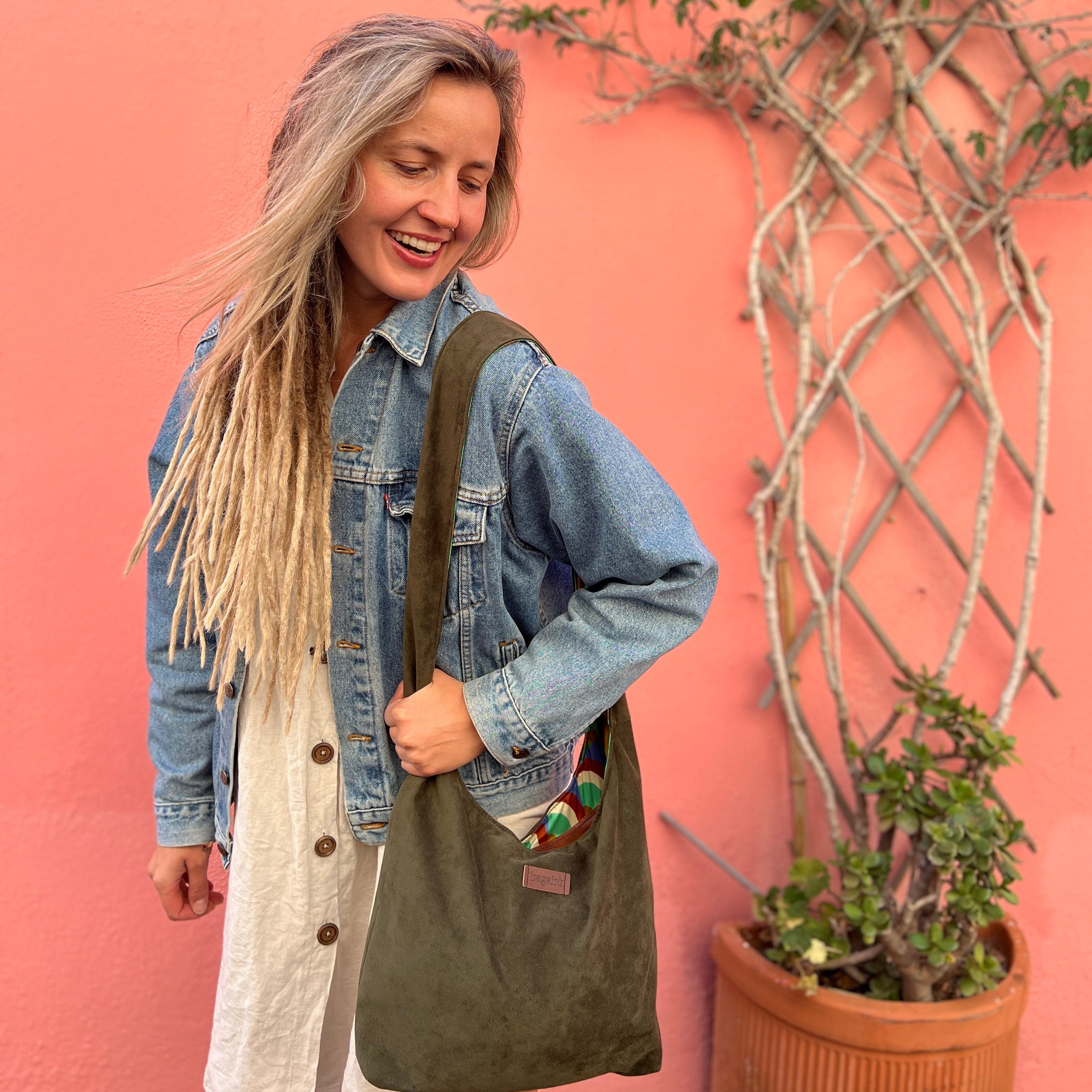 Woman holding a green bag against a pink wall with plants
