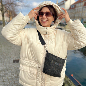 Woman in a white puffer jacket with a hood, sunglasses, and a black crossbody bag standing by a waterway.