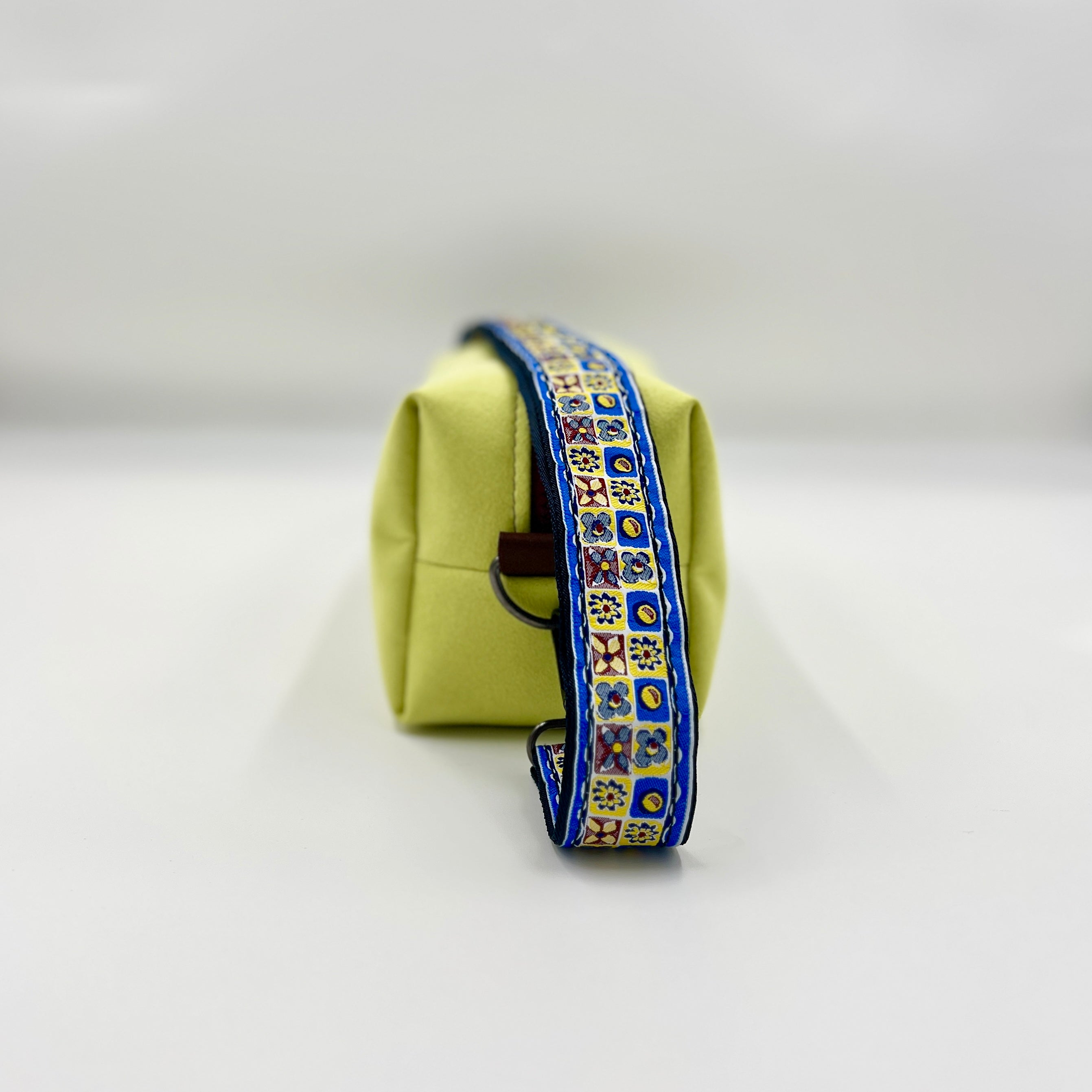 Light green toiletry bag with a decorative blue strap on a white background