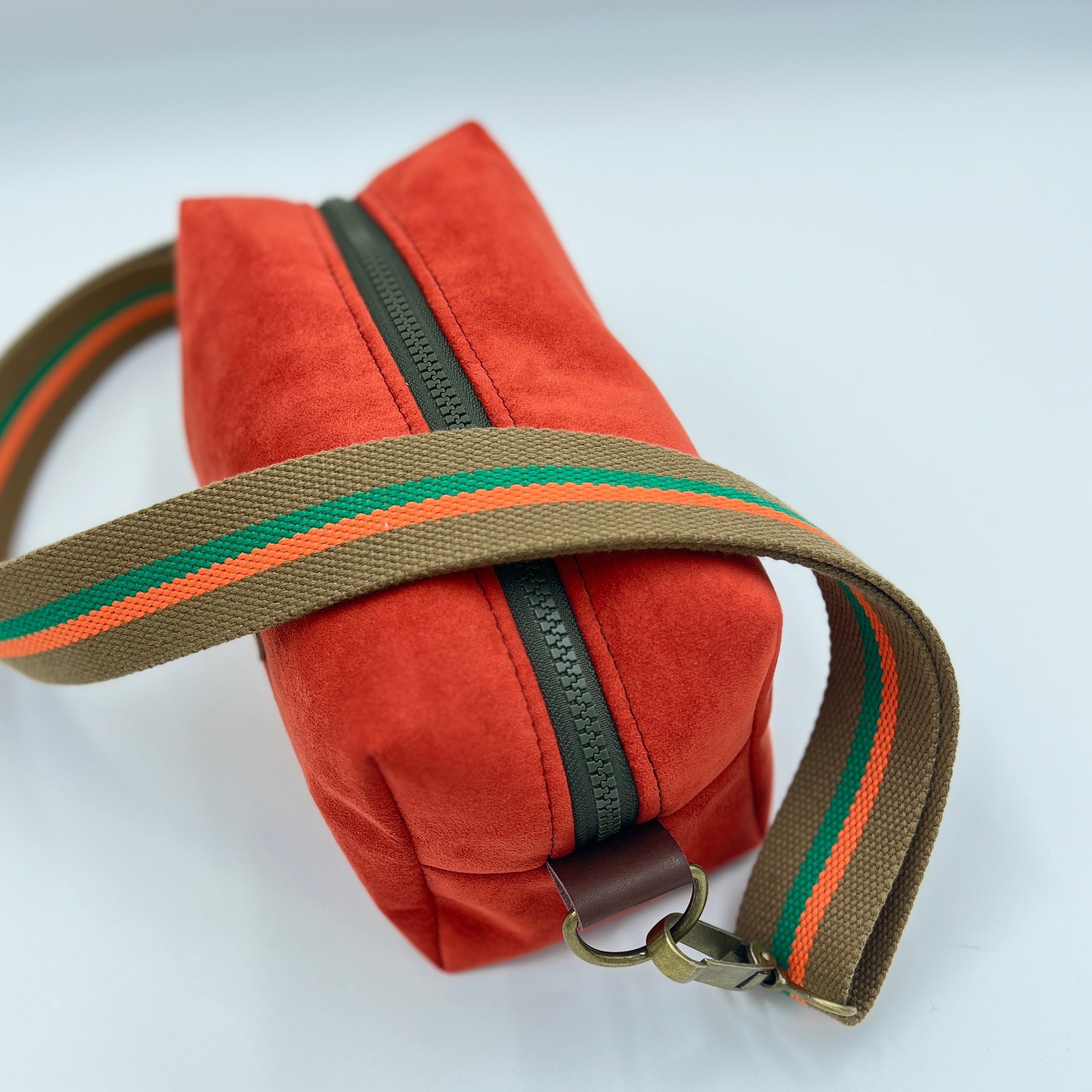 Orange bag with a brown strap featuring green and orange stripes on a white background