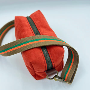 Orange bag with a brown strap featuring green and orange stripes on a white background