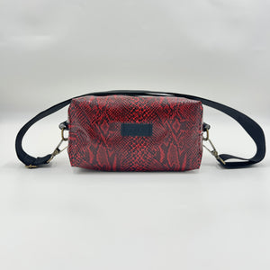 Red snake print bag with black strap on a light gray background